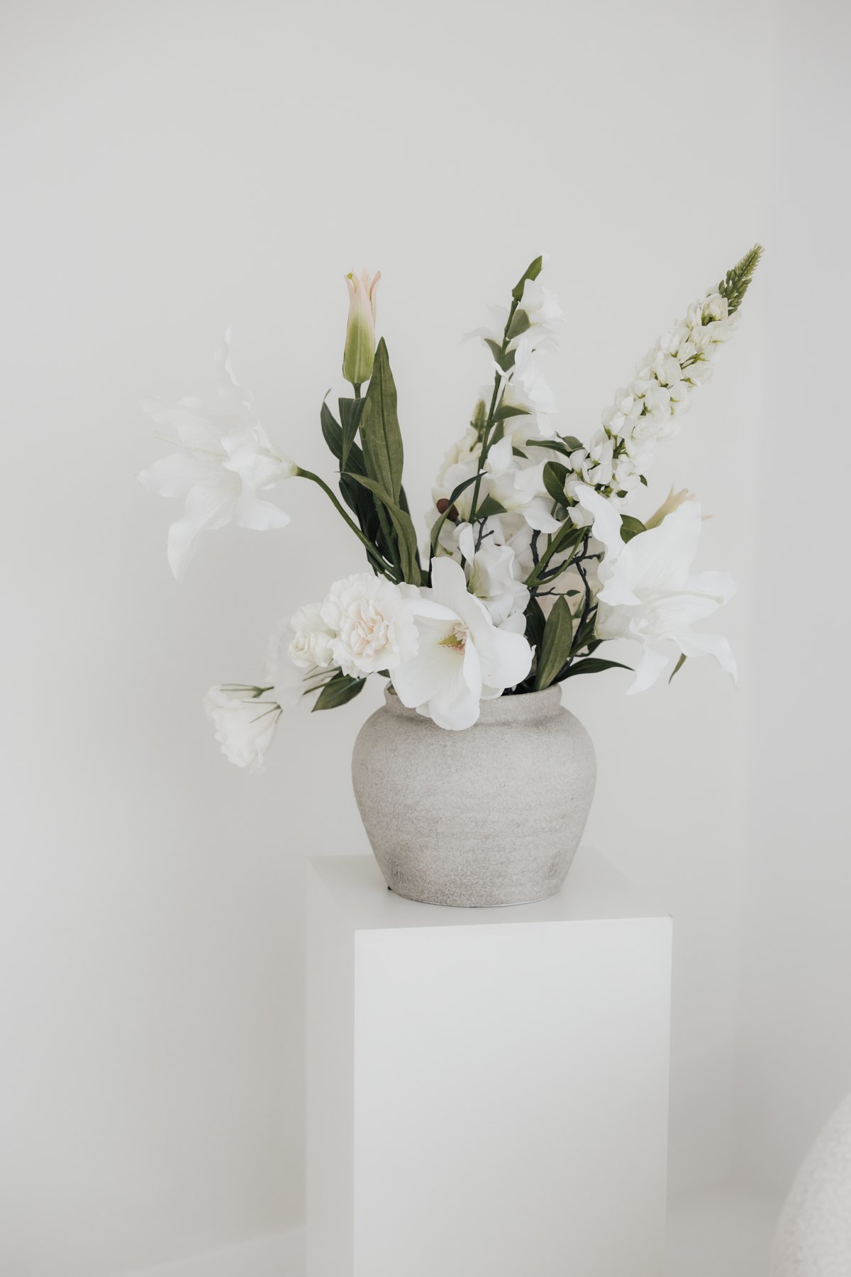 Weiße Blumen in einer Steinvase im hellen Tageslichtstudio